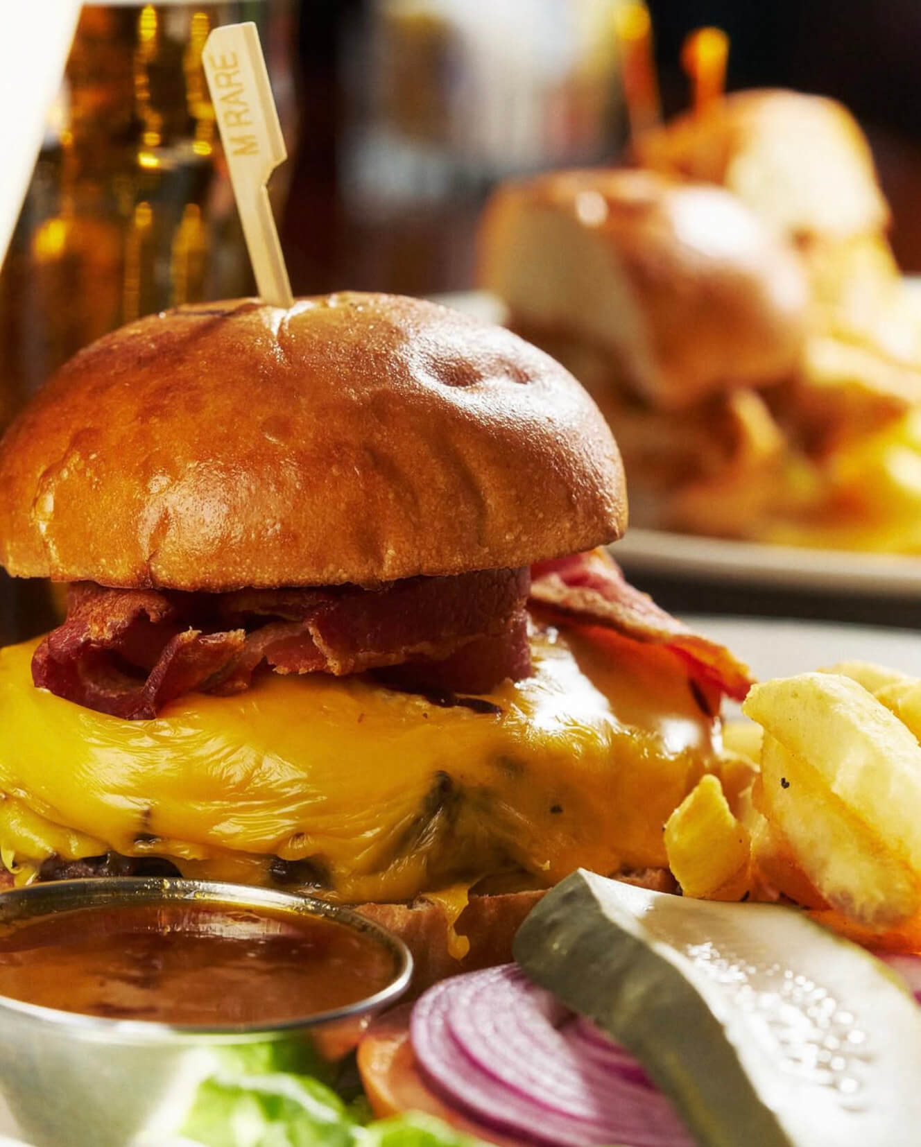 Cheeseburger with melted cheddar, crispy bacon, lettuce, tomato, red onion, pickle, and a side of fries and dipping sauce.